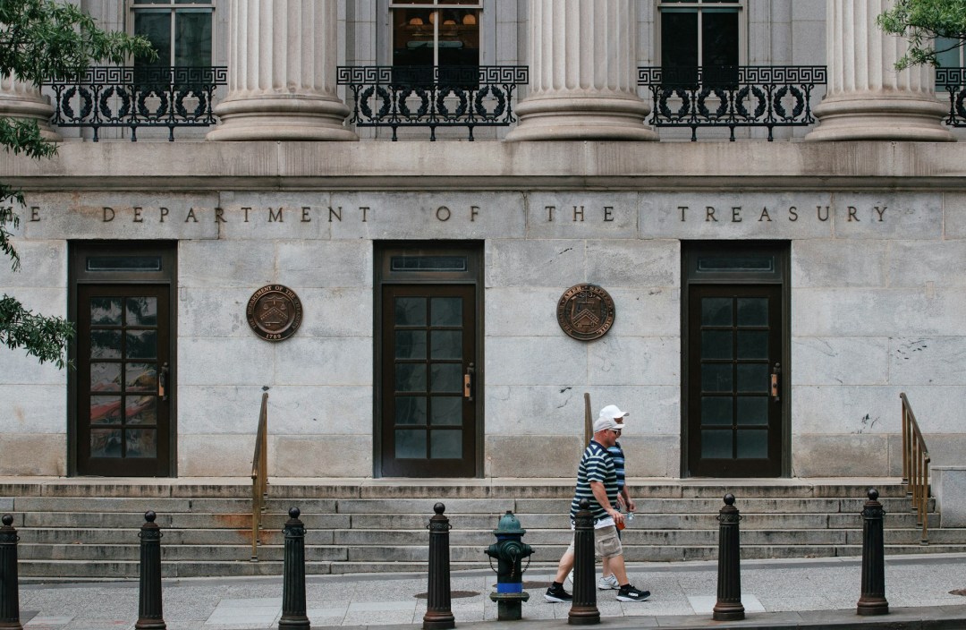 Exterior of the U.S. Treasury Department building in Washington, D.C., with a pedestrian walking past.